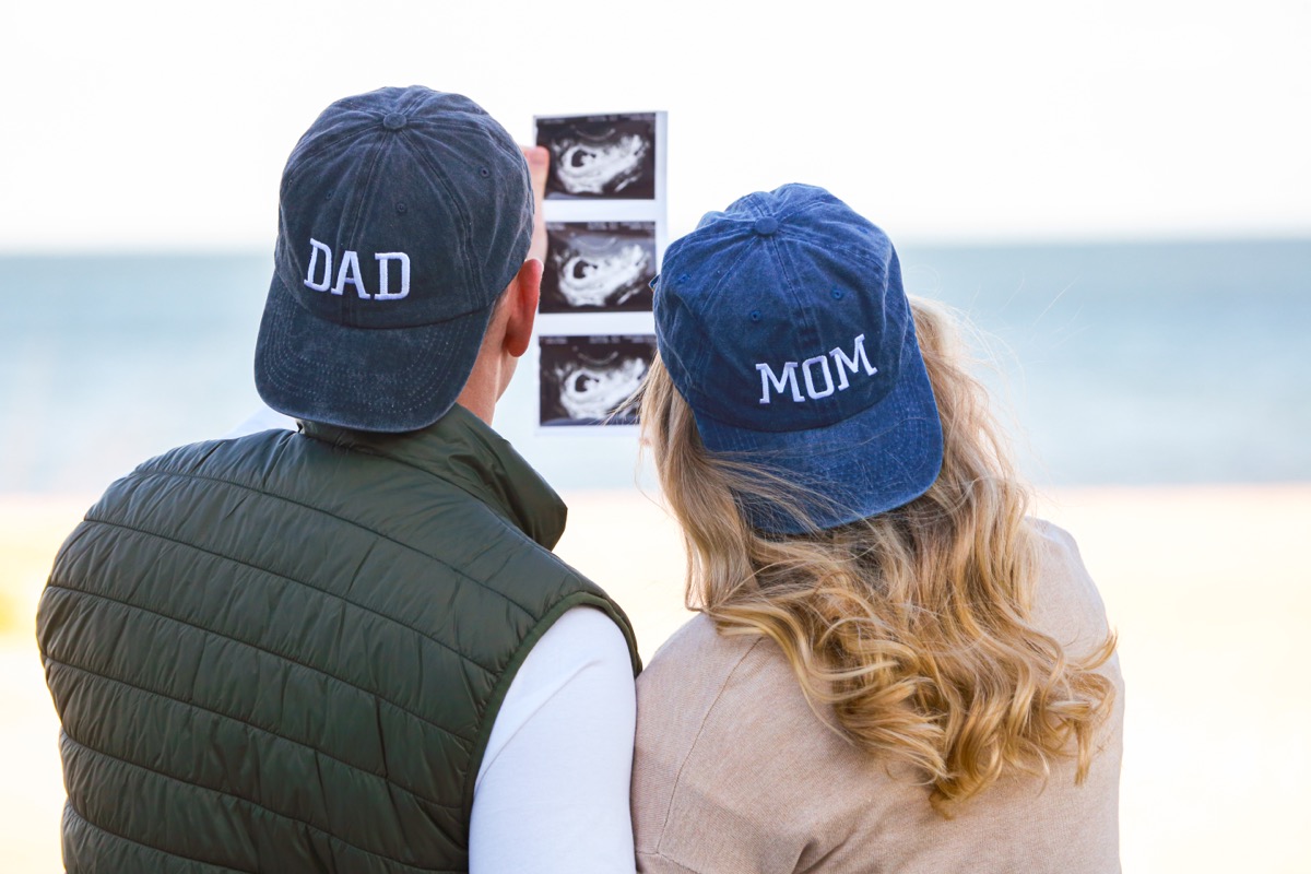 Man and woman wearing "mom" and "dad" hats holding ultrasound picture